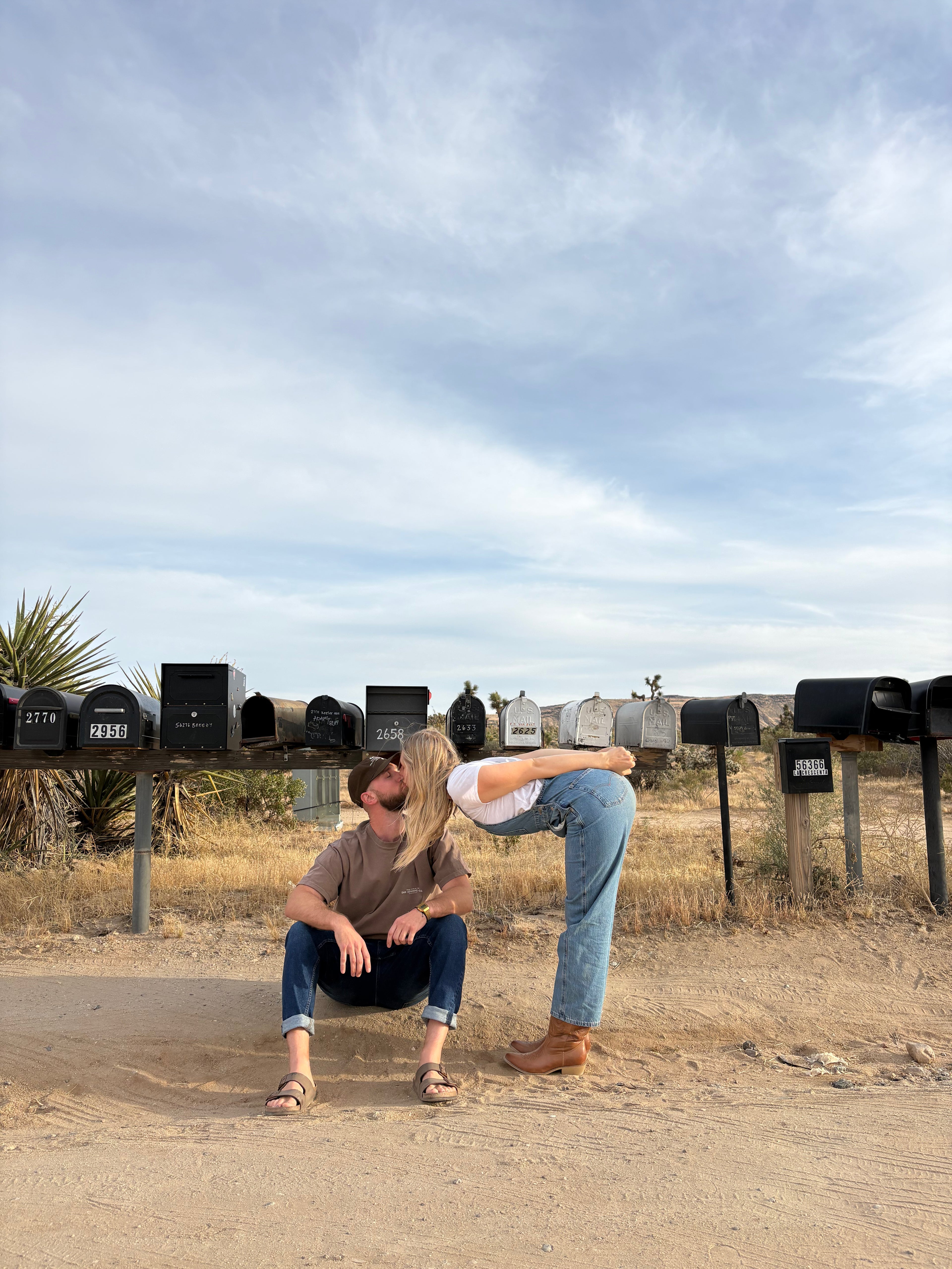 Two people embracing in a rural setting with mailboxes in the background.